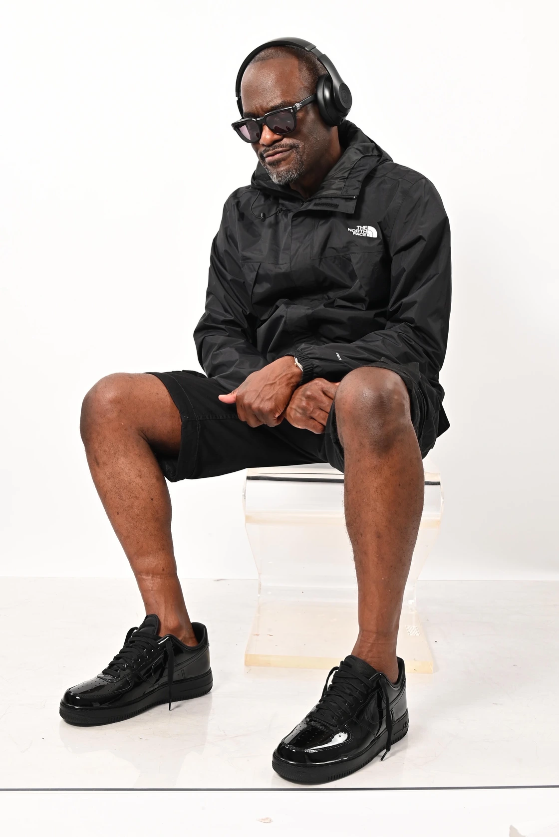 Glenn Toby seated wearing headphones, sunglasses, a black jacket and shorts