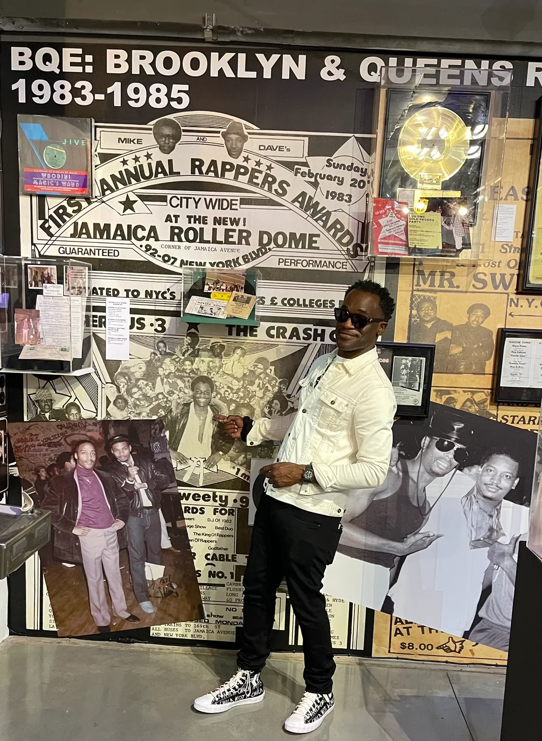 Dr. Glenn Toby at the Universal Hip Hop Museum, standing in front of a wall-sized reproduction of his First Annual Rappers Awards flyer